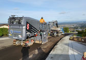 Contractors grind the top layer of road pavement.